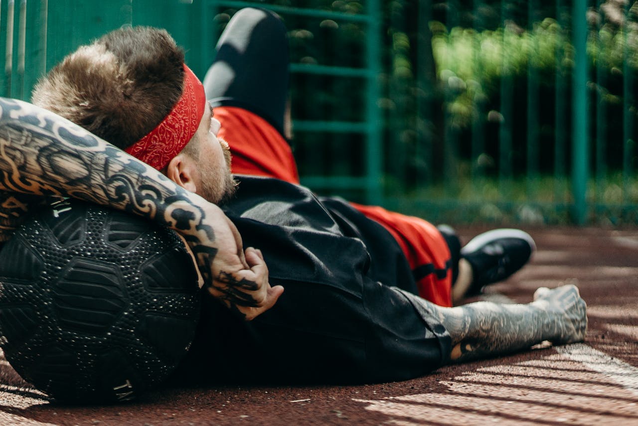 Tattooed man relaxes on basketball court with a ball, displaying athletic lifestyle.